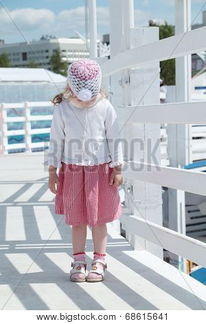 Little Cute Girl Stands On White Wooden Bridge And Looks Down