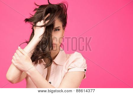 Beautiful woman holding her hair over pink background. Covering half face with hair. Looking at camera. 