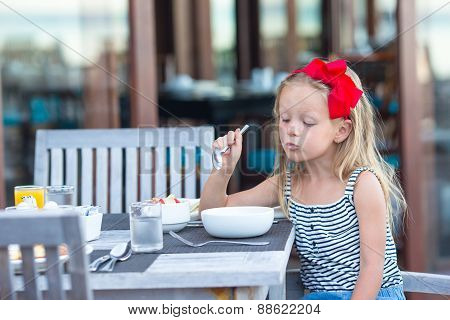 Adorable little girl eating porridge on breakfast at outdoor cafe