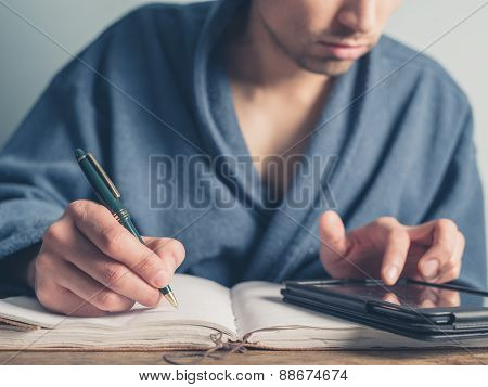 Man In Bathrobe Using Table And Taking Notes