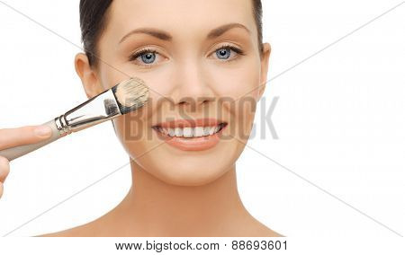 beauty and makeup concept - woman applying liquid foundation with brush