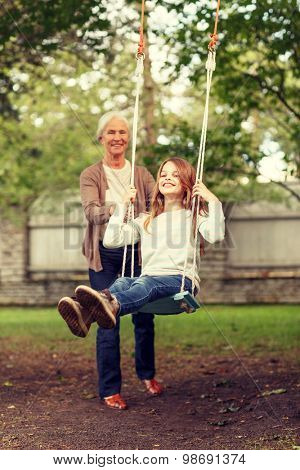 family, happiness, generation, home and people concept - happy grandmother and granddaughter swinging on teeterboard outdoors