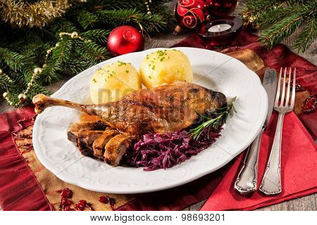 Crusty goose leg with braised red cabbage and dumplings on Christmas decorated table
