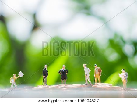 Tiny miniature models of businessman are standing on a pile of coins using as agreement investment achievement and partnership business concept.