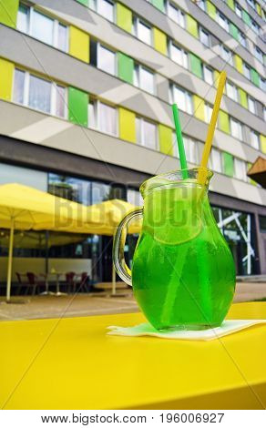 Glass of green estragon lemonade out of cafe, modern building on background. Summer refreshing cocktail with lime, estragon and vanilla.