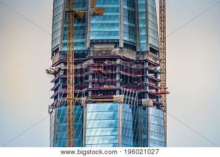 Detailed view of a skyscraper under construction with the cranes on the construction site.