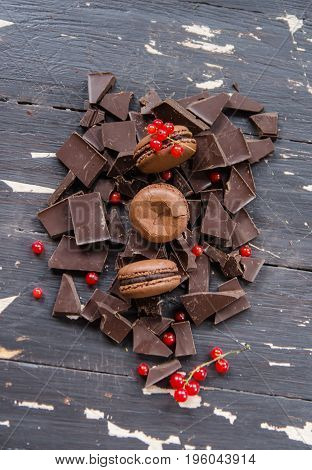 Delicious chocolate macarons over pieces of chocolate on wooden background. Top view.