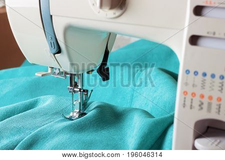 Close up of sewing machine working with turquoise fabric