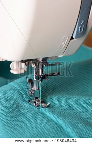 Close up of sewing machine working with turquoise fabric