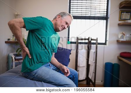 Side view of male patient suffering from back ache while sitting on bed at hospital ward