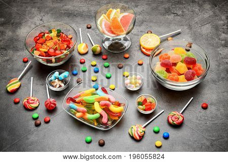 Bowls with delicious candies on grey background