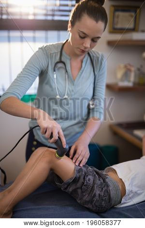 Young female therapist using ultrasound machine on knee of boy at hospital ward