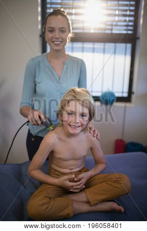 Portrait of smiling female therapist holding ultrasound machine with shirtless boy at hospital ward