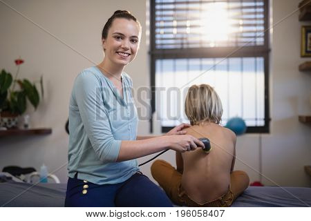 Portrait of smiling young female therapist using ultrasound on shirtless boy at hospital ward