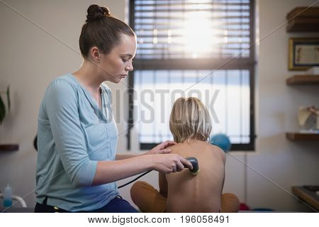 Female therapist using ultrasound machine on back of shirtless boy at hospital ward