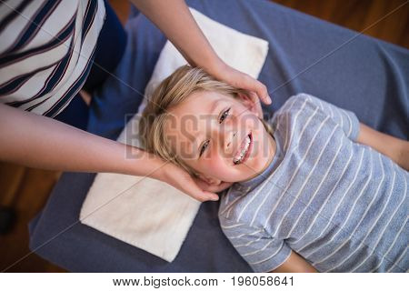 High angle portrait of smiling smiling boy receiving massage from female physiotherapist at hospital ward