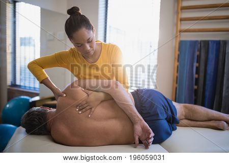 Senior male patient lying sideways on bed receiving back massage from female therapist at hospital ward