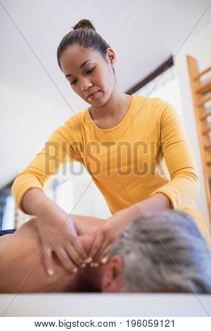 Low angle view of female therapist giving neck massage to male patient at hospital ward
