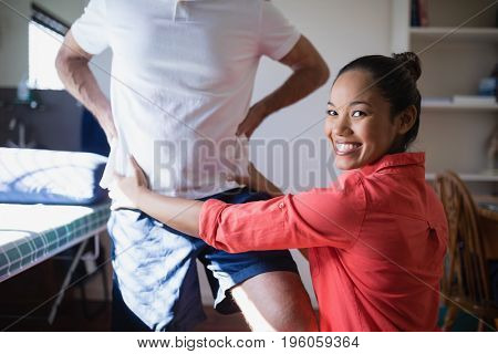Portrait of smiling female therapist massaging back at hospital ward