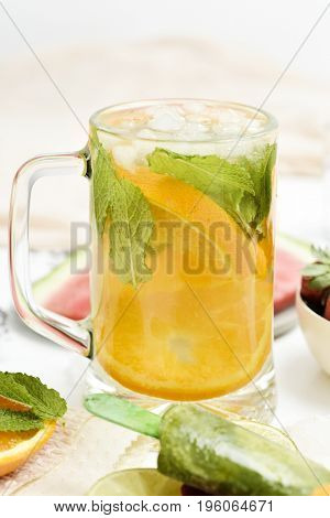a jar with a refreshing drink, with orange slices and mint, a bowl with strawberries, a plate with watermelon and a plate with some different homemade natural ice pops, placed on a set table