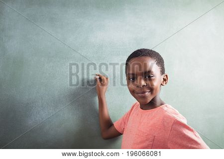 Portrait of boy standing by chalkboard in classroom
