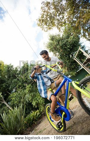 Tilt image of father assisting son for riding bicycle in yard against sky