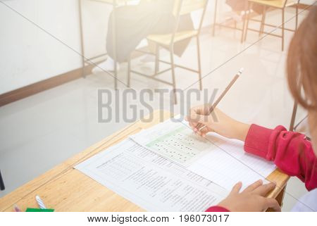 Asian Student hand holding pencil writing doing test examination and exams answer sheets in class room education exam concept