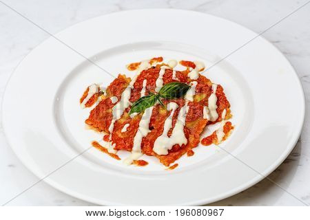 Ravioli with tomato sauce served in white plate on marble serface.