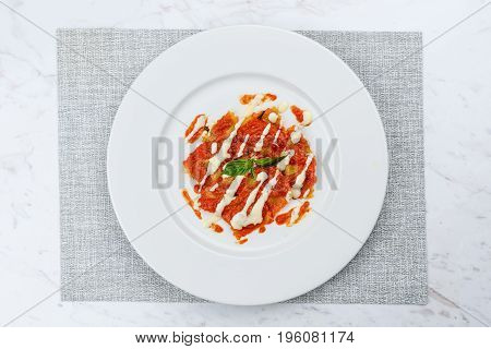 Ravioli with tomato sauce served in white plate on marble serface.
