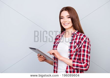 Succcessful Pretty Brunette Student Is Typing On Her Tablet, Standing In A Casual Checkered Shirt On