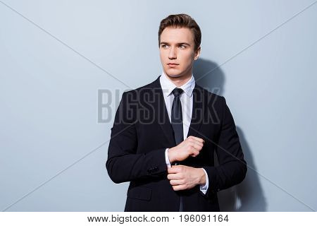 Young Handsome Businessman Banker In A Suit Is Fixing His Cuff Links, He Stands On Pure Light Backgr