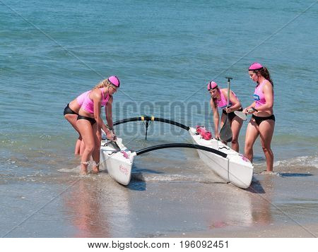 Mount Maunganui, New Zealand - January 28, 2012;  Four women in pink tops returning to beach from surf with outrigger canoe in paddling competions at Mount Maunganui Surf Lifesaving 2012.