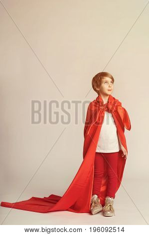 Super hero girl in red cape posing in studio. Child in superwoman costume