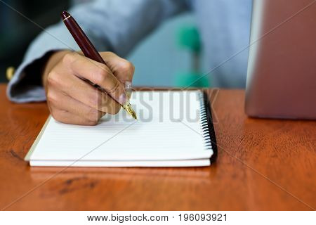 Beautiful Asian businesswoman is taking notes on her notebook while using the tablet in her office. Finance Banking and Technology Concepts.