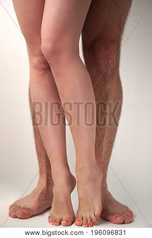 Smooth female and hairy male feet on a light background. Sexual overtones.