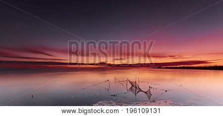 Fishnets in a calm and quiet sea under a bright red dawn