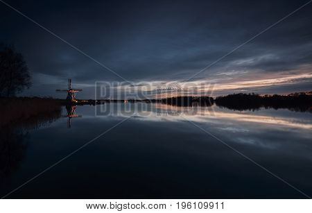 Illuminated Dutch windmill at an orange sunset reflected in a quiet lake