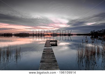 Empty wooden platform with reed in a calm lake under an orange and purple sunset