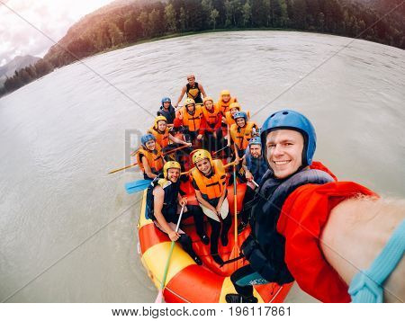 mountain Altai, RUSSIA - July 16, 2017: man in a helmet holds an action camera and makes selfie on the background of friends with oars, rafting