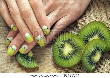 Kiwi and skin care of a beauty female hands with green and white moon nail art manicure on a sackcloth and wooden background