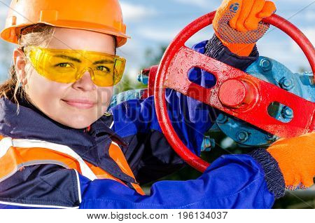 Woman worker in the oilfield repairing wellhead, wearing orange helmet and work clothes. Industrial site background. Oil and gas concept.