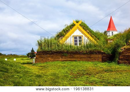 Church bell tower with a peaked red roof in old village of  houses covered with turf. Ethnographic Museum-estate Glaumbaer, Iceland. The concept of the historical and cultural tourism