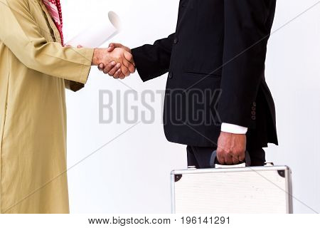 Arab business man shake hand with Asian business man in the blakc suit carrying a silver suit case.