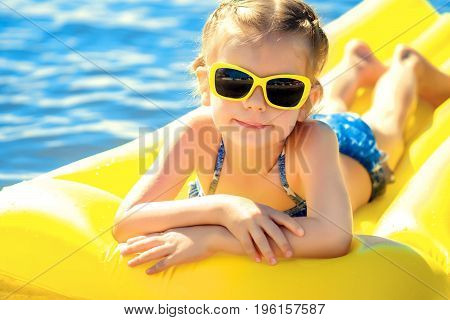 Little girl in sunglasses swimming on inflatable beach mattress.