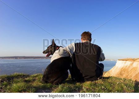 Rear view of a man and dog sitting on beach. man holding his loyal dog