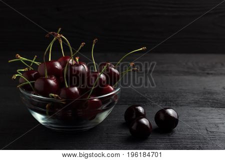 Cherry In A Glass Plate On A Black Wooden Background