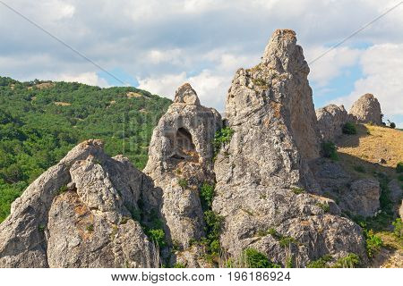 The mountain is an unusual form with a grotto in the background of hills with forests and a cloudy sky. Delikli-Kaya rock peninsula of Crimea