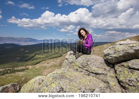 Woman Sitting On Top Of Mountain Typing In Tablet