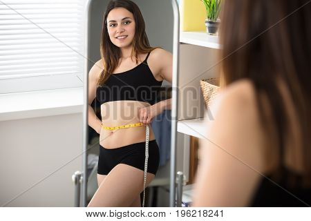 Close-up Of A Woman's Reflection In Mirror Measuring Her Belly