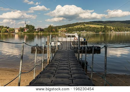 A barrel jet leading to the boat. Background view on village Frymburk Lipno lake Czech Republic. Frymburk in sunny day view from Frydava port.